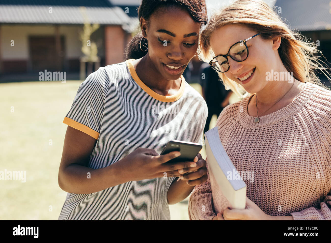 Two young women at college campus looking at mobile phone. High school girls walking in university campus with smart phone. Stock Photo