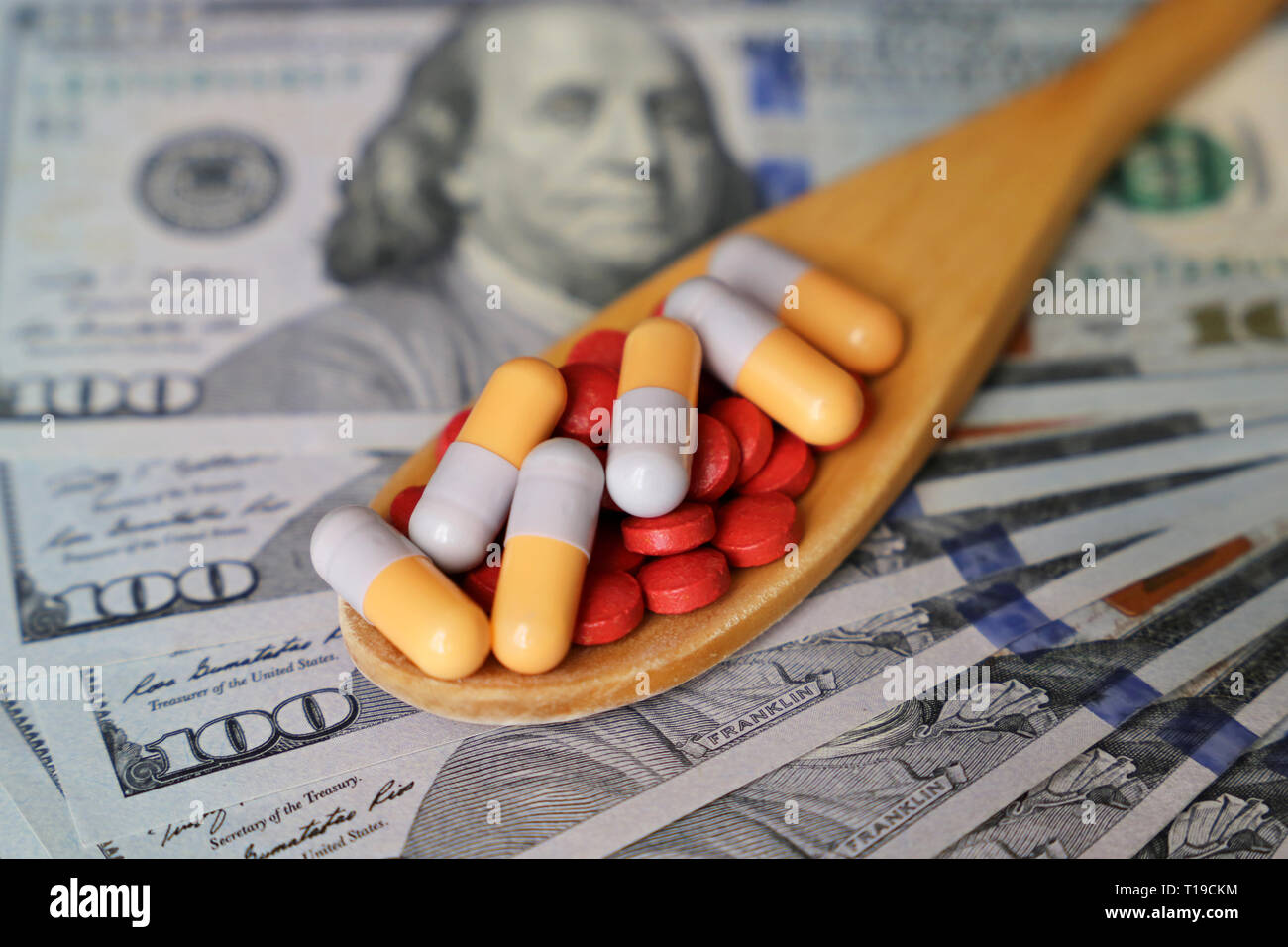 Pills and capsules in wooden spoon on US dollars bills. Concept of health care, pharmaceutical