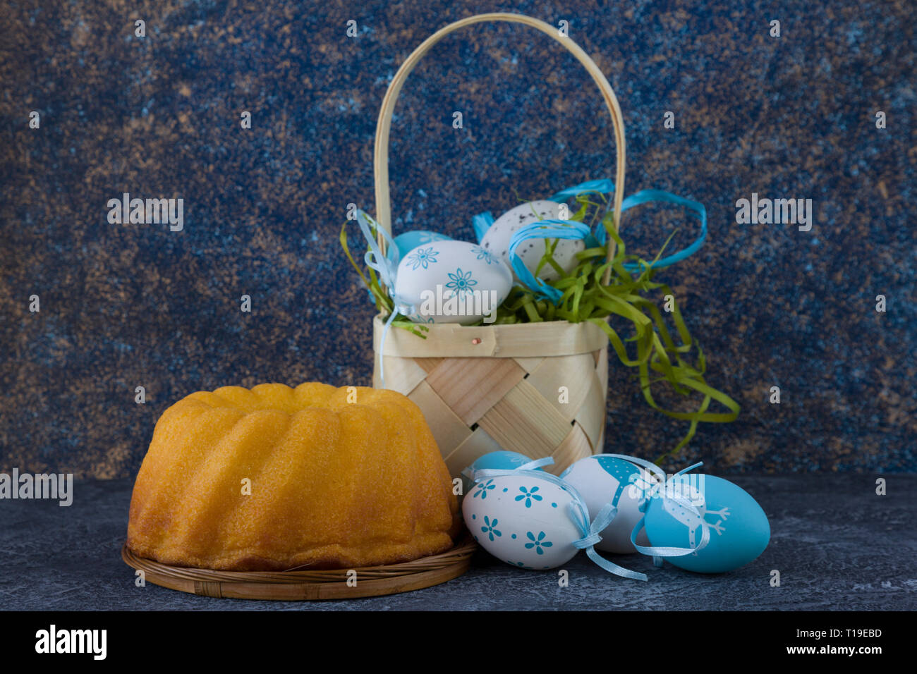 Easter bread and painted Easter eggs in a basket on dark stone table Stock Photo