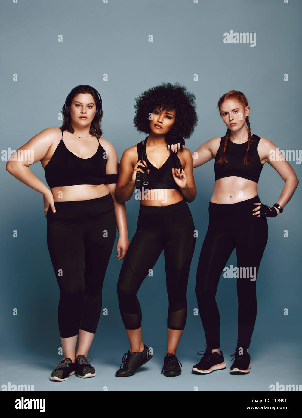 Group of multi-ethnic women in sportswear standing together over grey  background. Three women of different race, figure type and size in fitness  cloth Stock Photo - Alamy