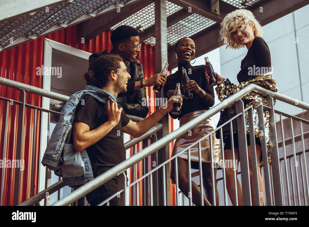 Group of young friends hanging out on weekend. Multiracial men and women standing on steps having soft drinks. Stock Photo