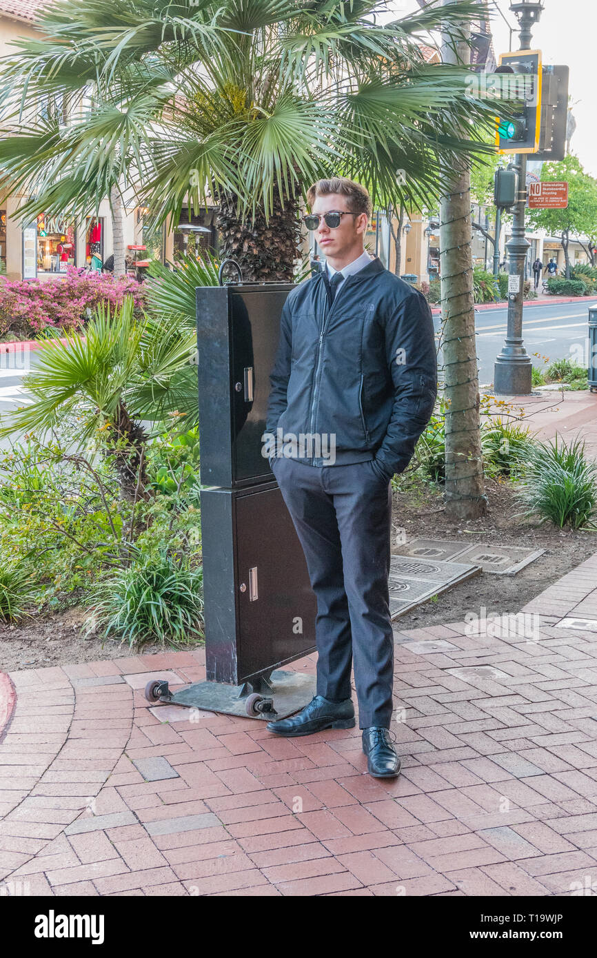 A young adult valet, dressed in all black, stands by his moveable valet