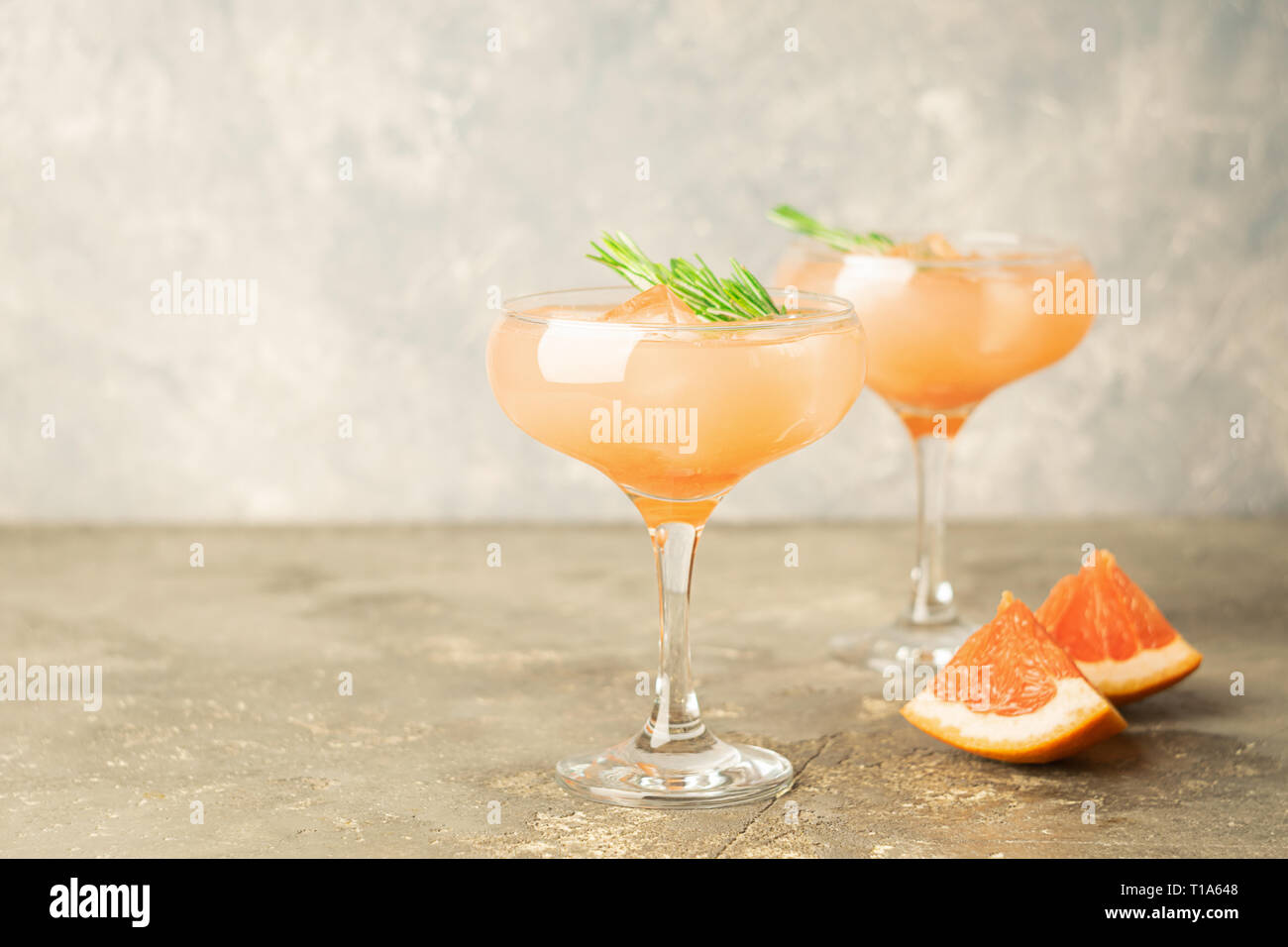 Drink grapefruit rosemary and ice two elegant glass goblets on gray ...