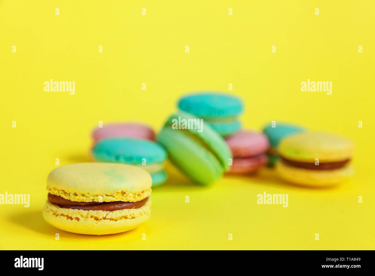 Sweet almond colorful unicorn pink blue yellow green macaron or macaroon dessert cake isolated on trendy yellow modern fashion background. French swee Stock Photo