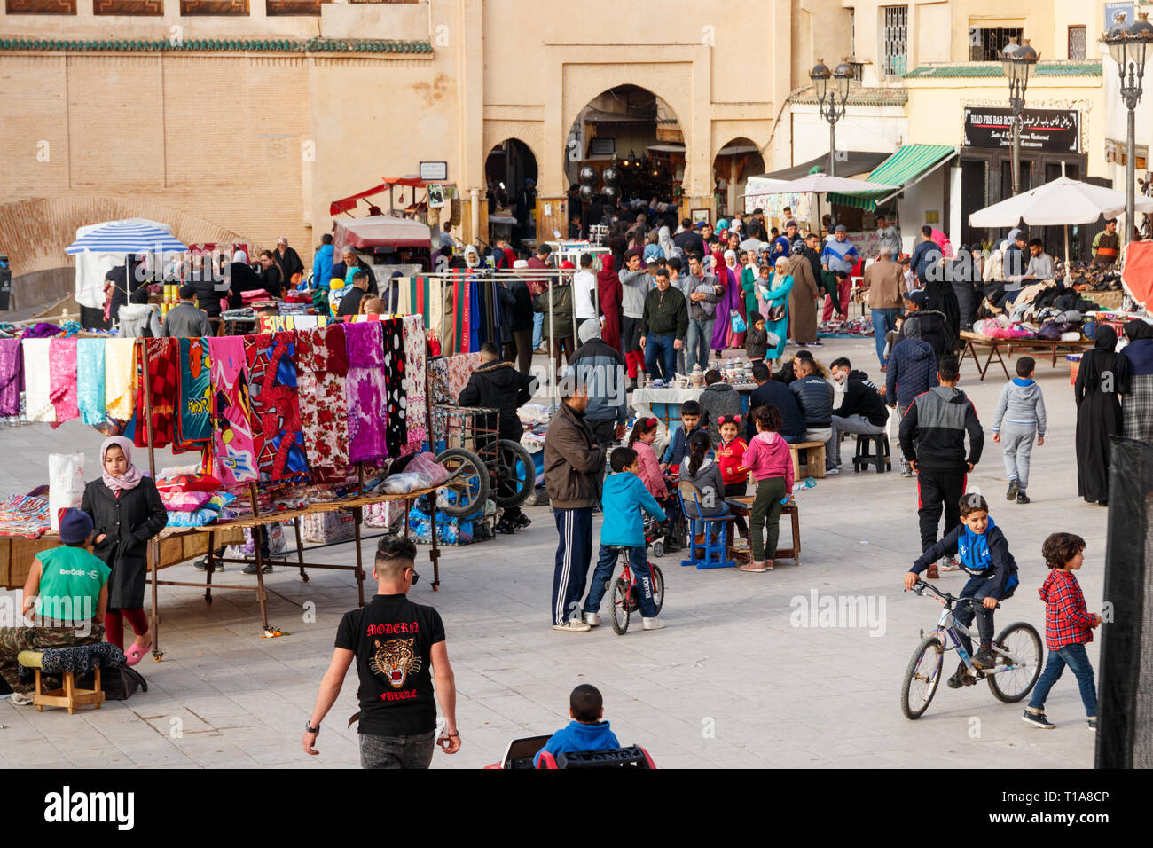 People at the market and children playing at Rcif square with a gate to the old medina at the background. Fez, Morocco. Stock Photo