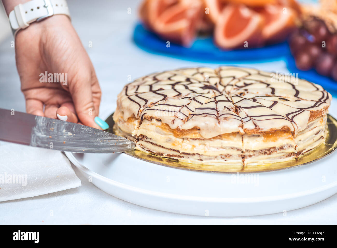 Woman's hands cut whole esterhazy torte cake with knife. Authentic recipe, hungarian and austrian dessert, view from above, close-up Stock Photo