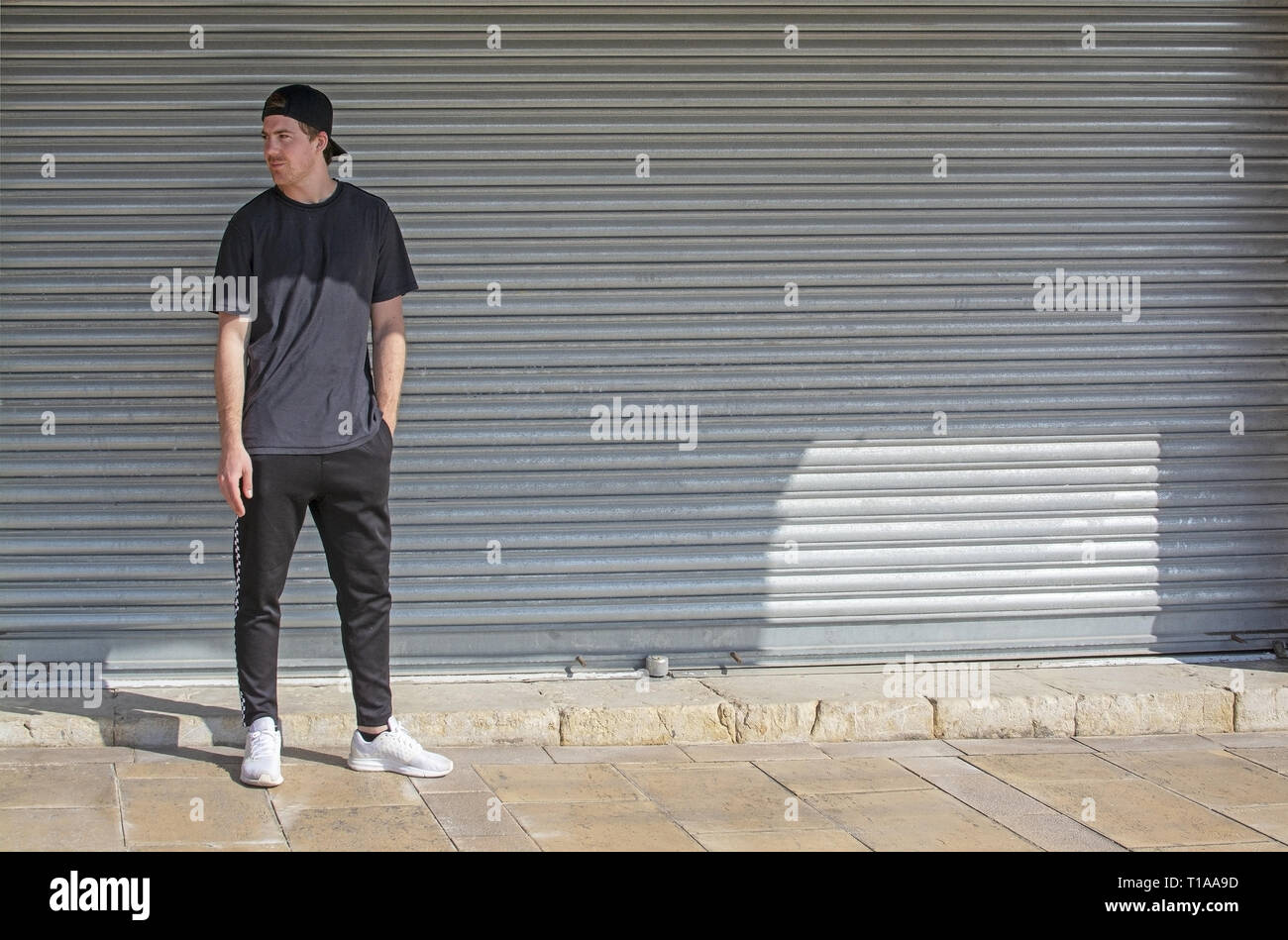 Young casual sporty dressed man with cap backwards in black against corrugated iron wall street style Stock Photo