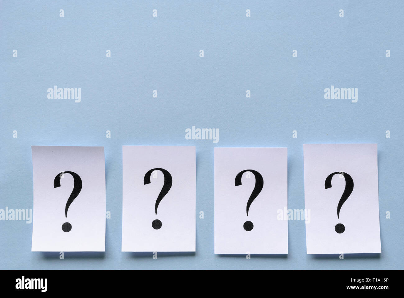 Four printed question marks on white paper forming a lower border on a blue background neatly laid in a row with three dimensional drop shadow and cop Stock Photo