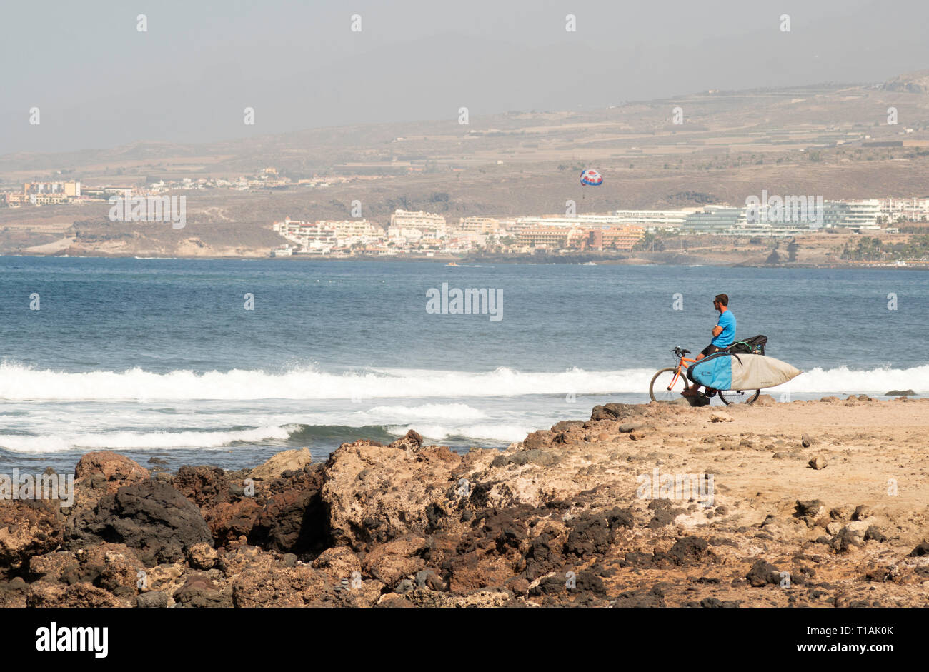 Surfer on bicycle looking out to sea in Costa Adeje, Tenerife, Canary Islands Stock Photo