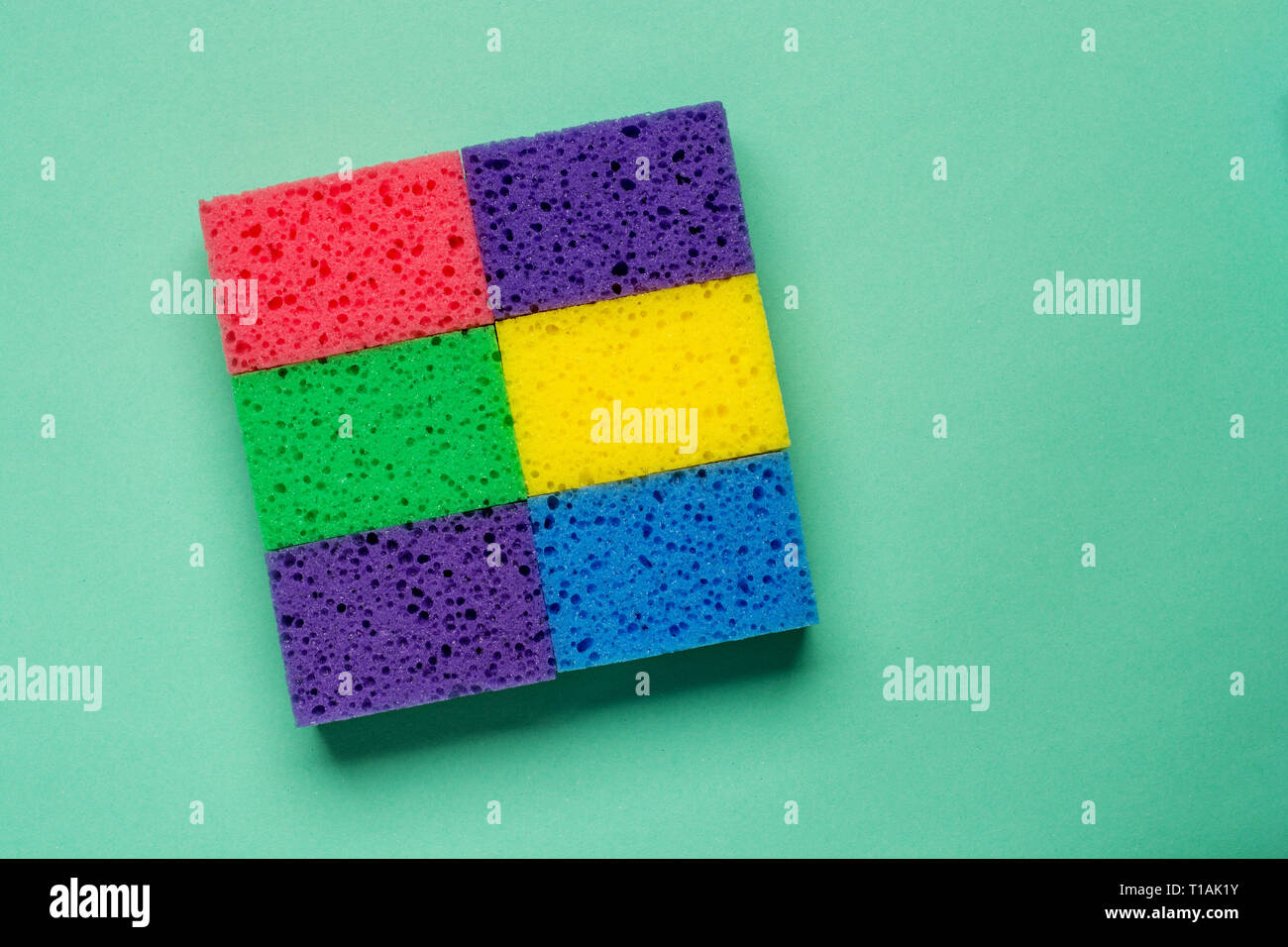 Set multi-colored sponges on a green background, space for text. Flat lay. Stock Photo