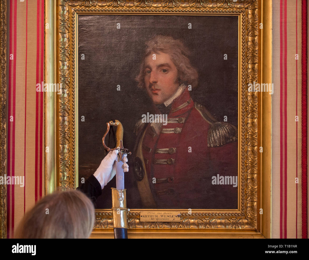 Apsley House, London, UK. 25 March, 2019. ‘Young Wellington in India’ exhibition explores the early years and provide insights into the man known globally as the 1st Duke of Wellington, who later defeated Bonaparte at Waterloo in 1815. The exhibition runs from 30 March - 3 November 2019. Image: Josephine Oxley, Keeper of the Wellington Collection, unsheaths an Indian sword from Wellington’s collection, alongside a portrait of Arthur Wellesley in the 33rd Regiment uniform. Credit: Malcolm Park/Alamy Live News. Stock Photo