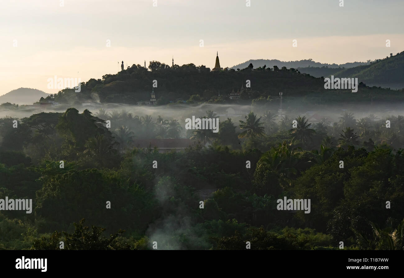 Krong Pailin, Cambodia. Sunrise and smoke from cooking fires hang in the still air over Pailin. Buddha and Wat Phnom Yat are silhouetted on horizon. Stock Photo