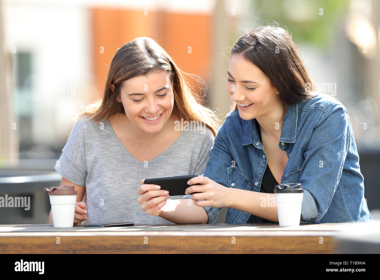 Two happy women watching online media on smartphone sitting in a park Stock Photo