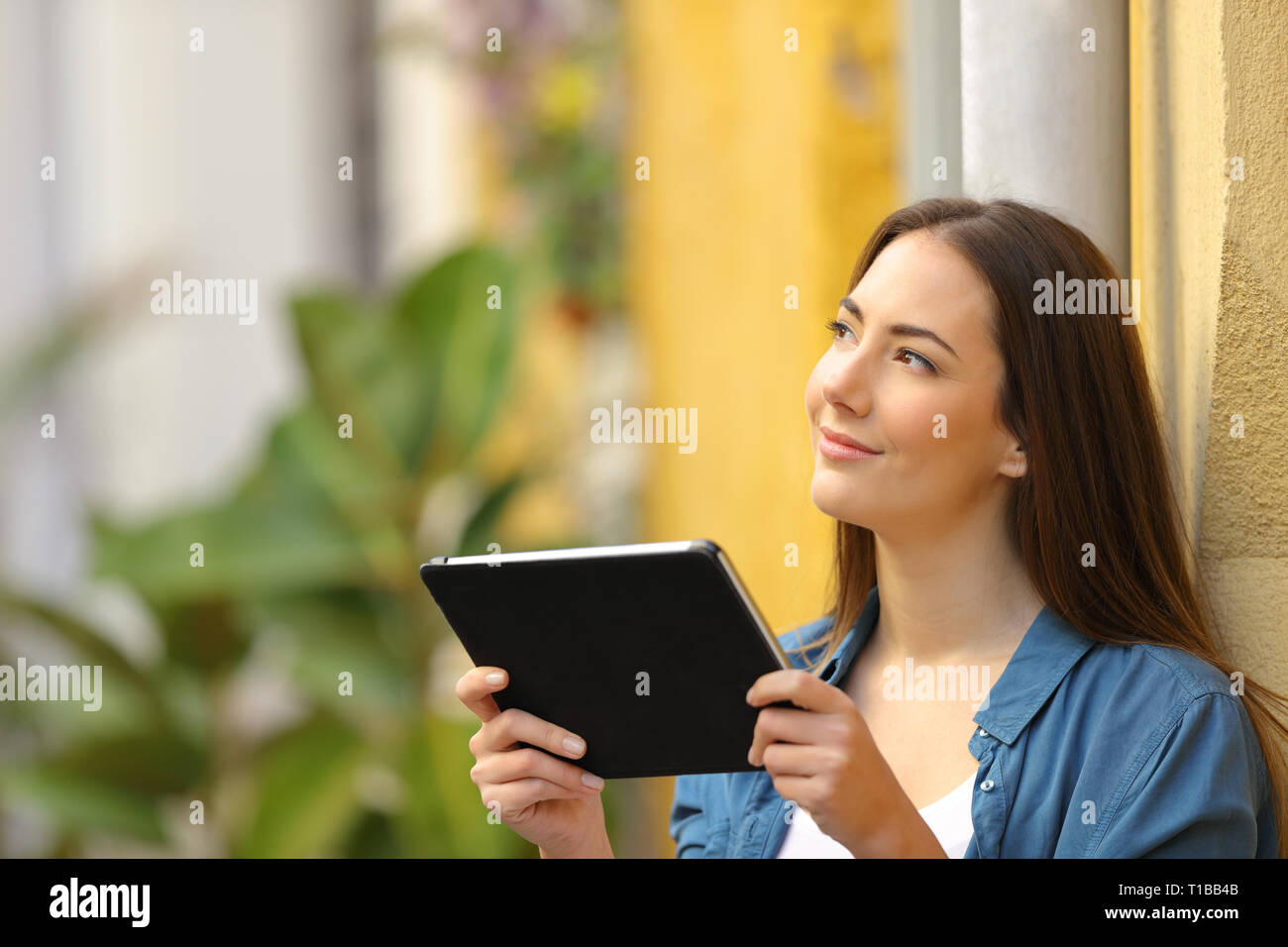 Woman holding a tablet thinking looking at side in the street Stock Photo