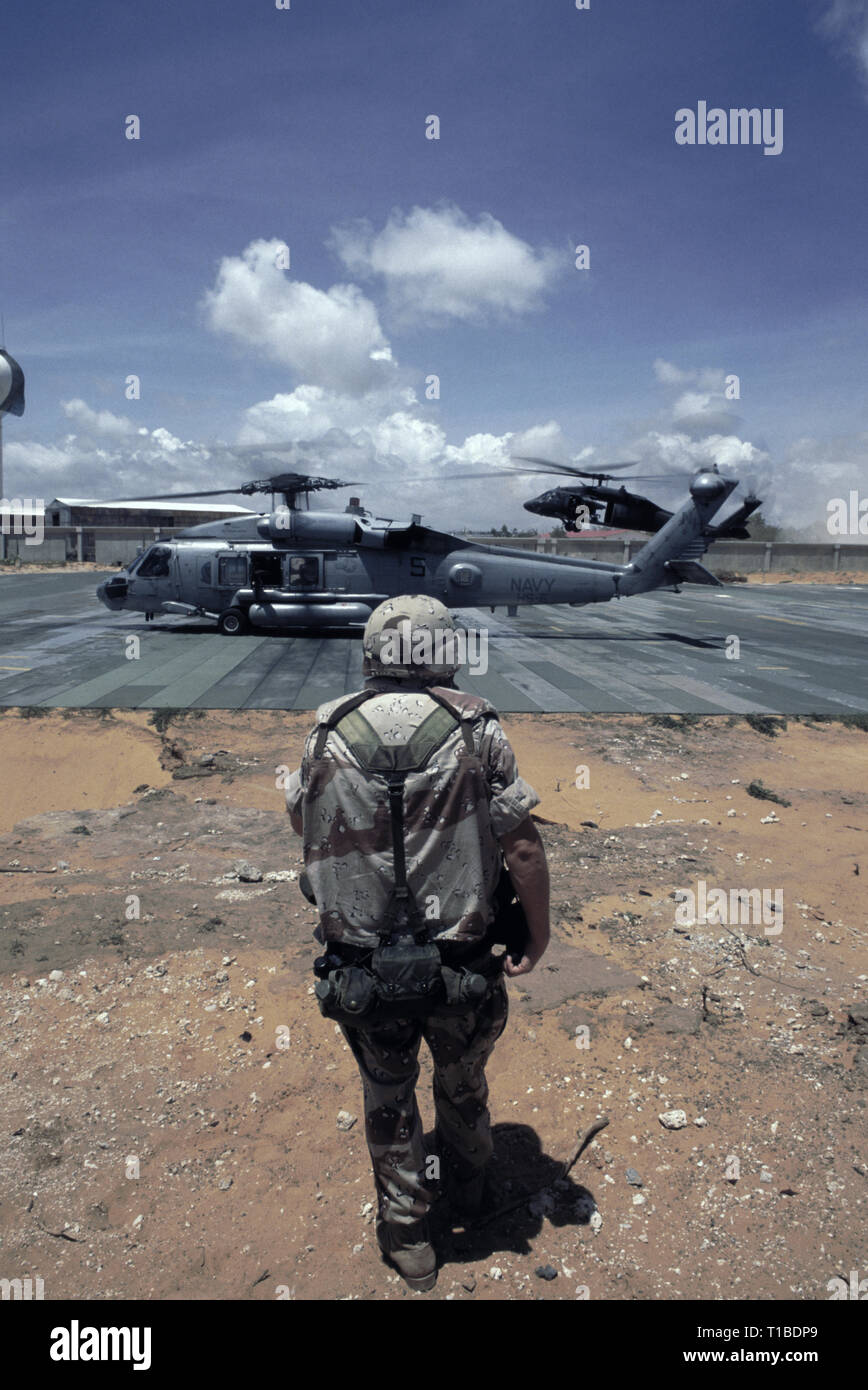 29th October 1993 A U.S. Army soldier stands in the foreground as a US Navy Sikorsky SH-60 Seahawk helicopter from the USS Abraham Lincoln prepares to take-off from the heli-pad at UNOSOM HQ in Mogadishu, Somalia. In the background, a US Army UH-60 Black Hawk helicopter is about to land. Stock Photo