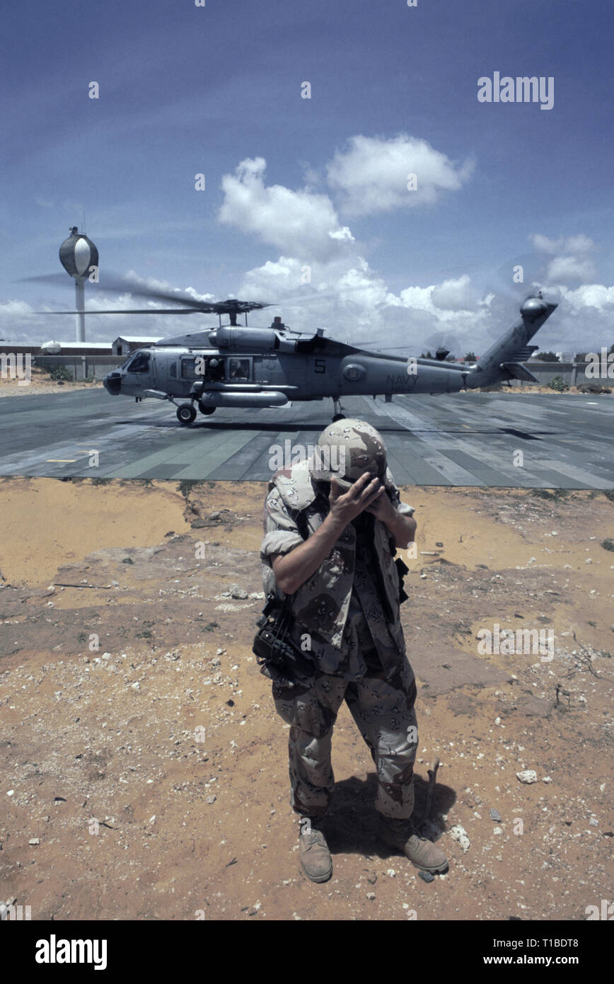 29th October 1993 A U.S. Army soldier turns his back to the sandstorm as a US Navy Sikorsky SH-60 Seahawk helicopter from the USS Abraham Lincoln takes off from the heli-pad at UNOSOM HQ in Mogadishu, Somalia. Stock Photo