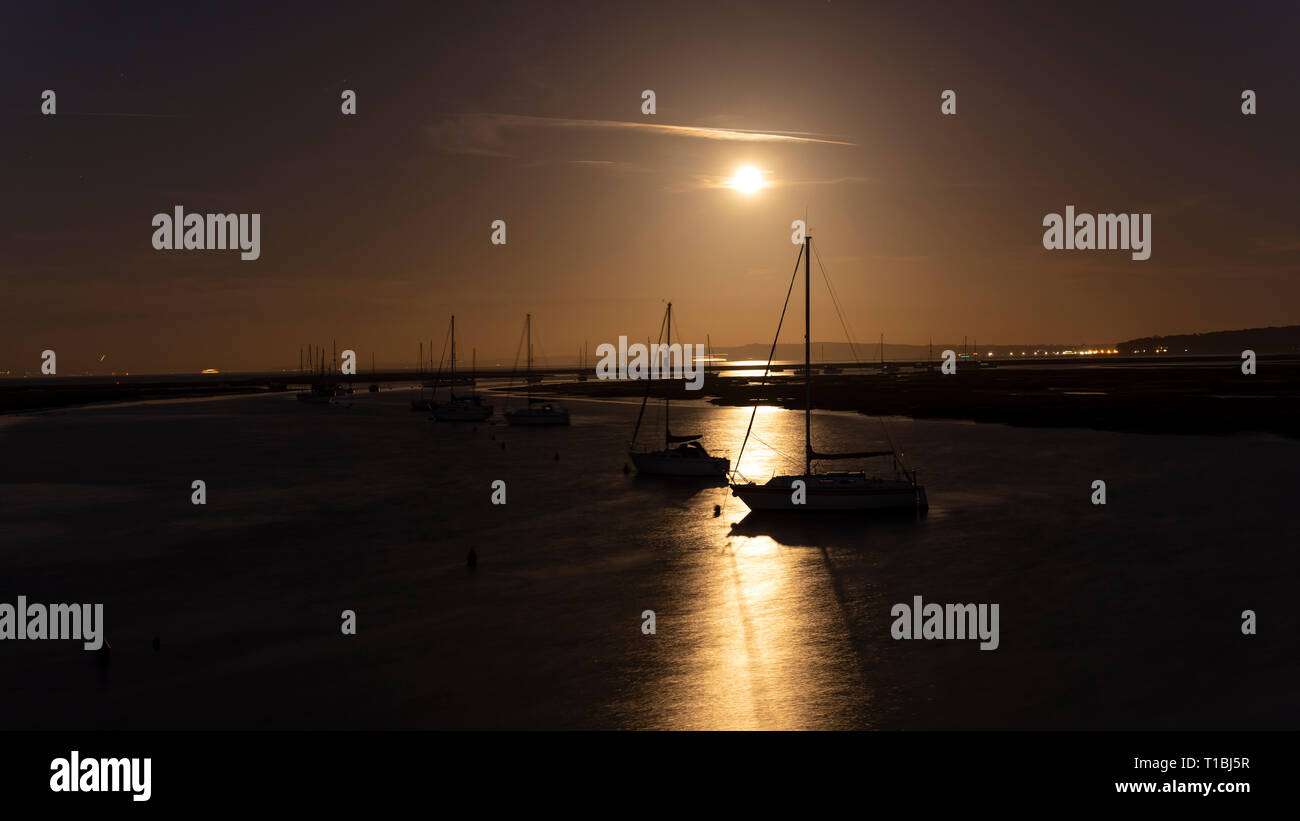 Sailing ships in the bay of keyhaven and full moon rising early in the night, England. Stock Photo
