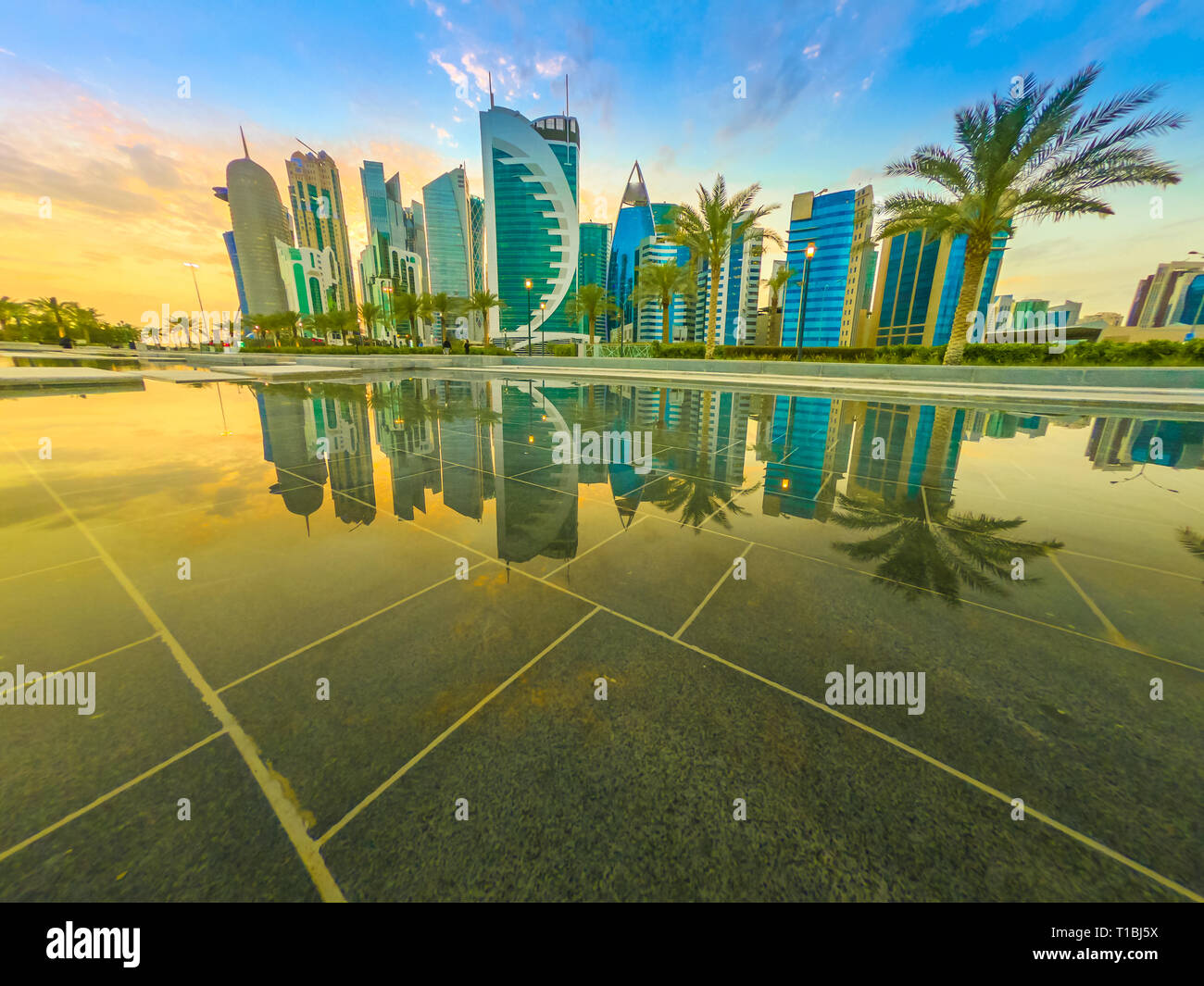Skyline of Doha, Qatar at sunset sky. Scenic cityscape of West Bay skyline miroring in the water of downtown park. Middle East, Arabian Peninsula in Stock Photo