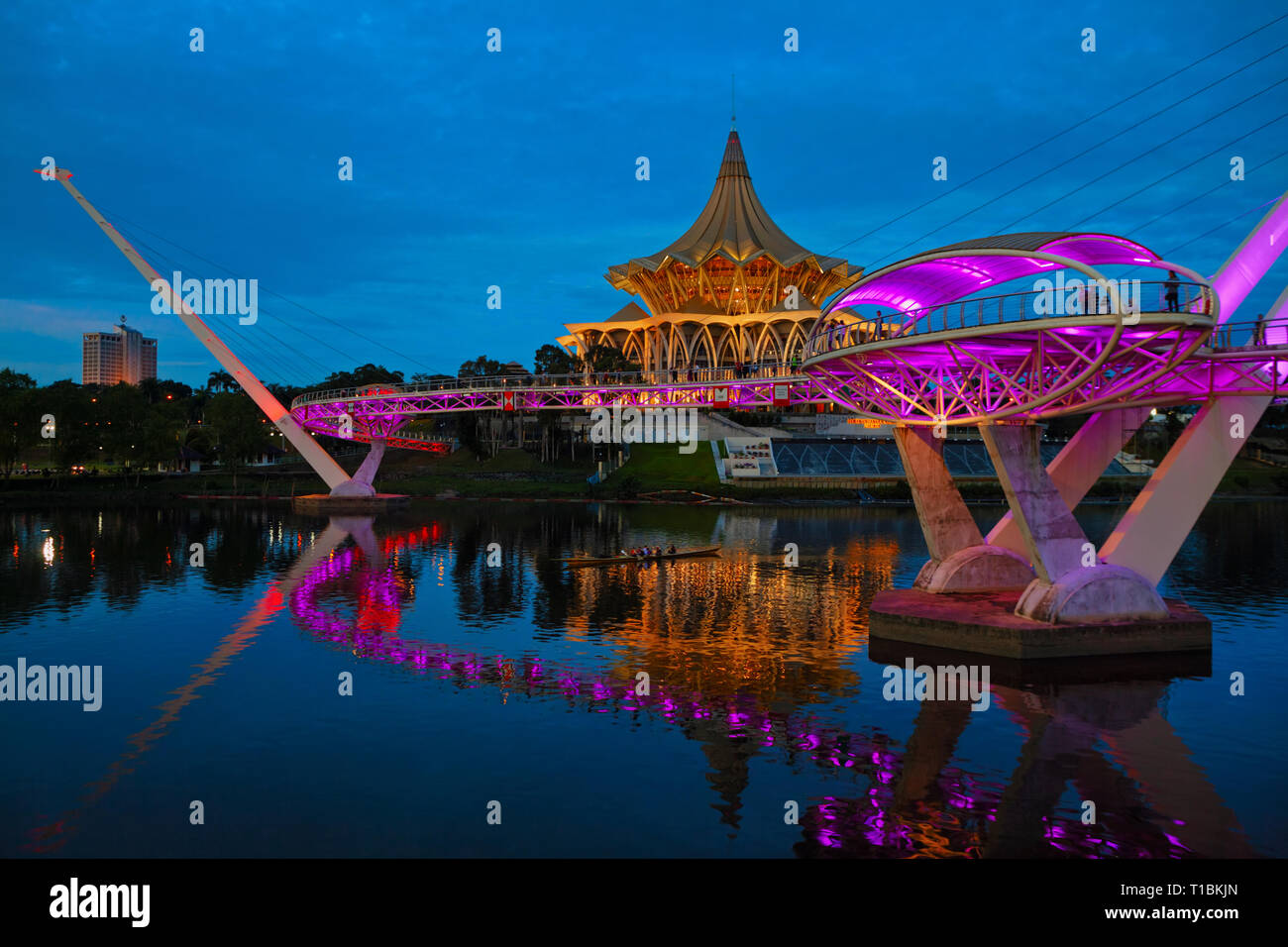 Kuching, Malaysia - March 11, 2019: Scenic night view of illuminated State Legislative Assembly and pedestrian bridge on Sarawak river. Stock Photo