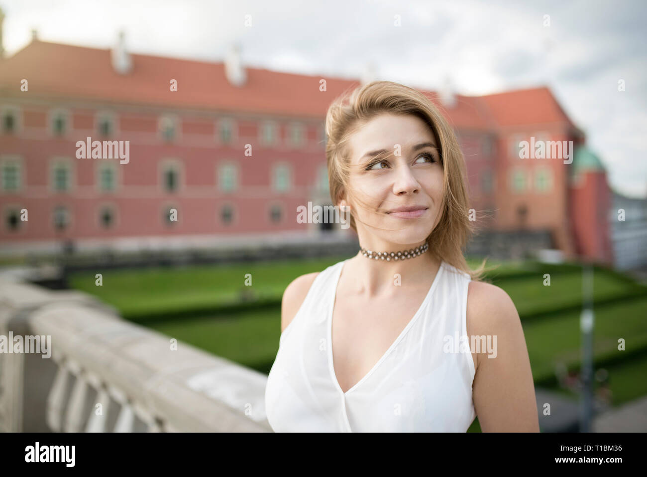 Portrait of smiling young adult woman, with short hair on windy day, looking in sky. On blurred background building from red brick. Old town. Stock Photo