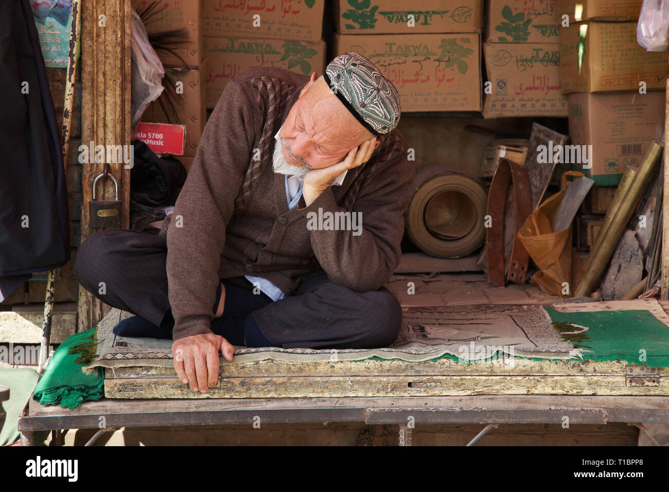 Old uighur shopkeeper fell asleep in front of his store, Kashgar Old Town, Xinjiang Autonomous Region, China. Stock Photo