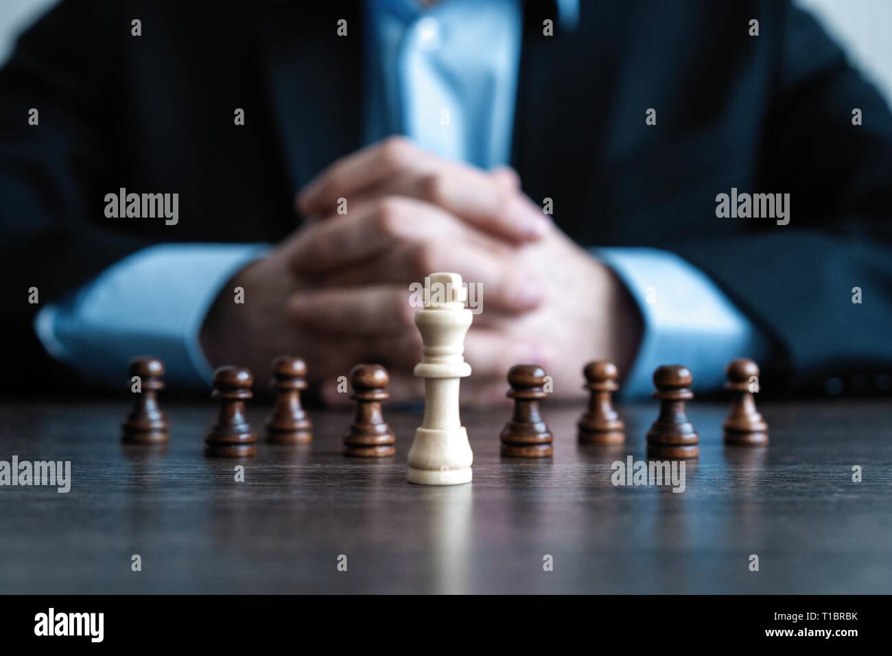Businessman with clasped hands planning strategy with chess figures on table. Strategy, leadership and teamwork concept Stock Photo