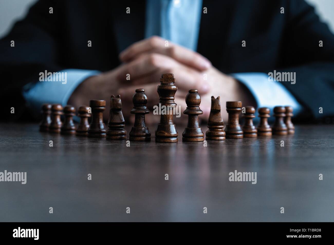 Businessman with clasped hands planning strategy with chess figures on table. Strategy, leadership and teamwork concept Stock Photo