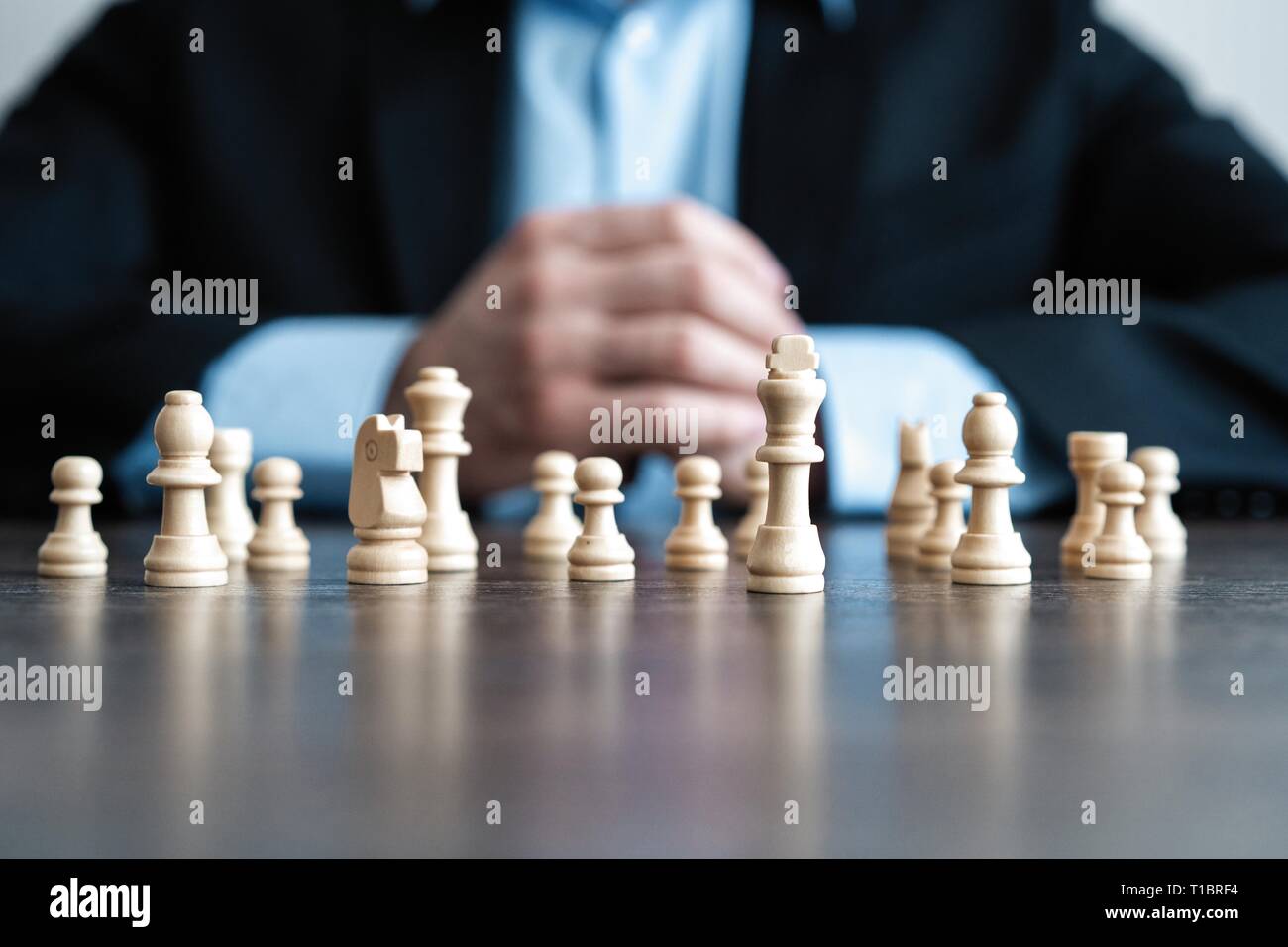 Businessman with clasped hands planning strategy with chess figures on table. Strategy, leadership and teamwork concept Stock Photo