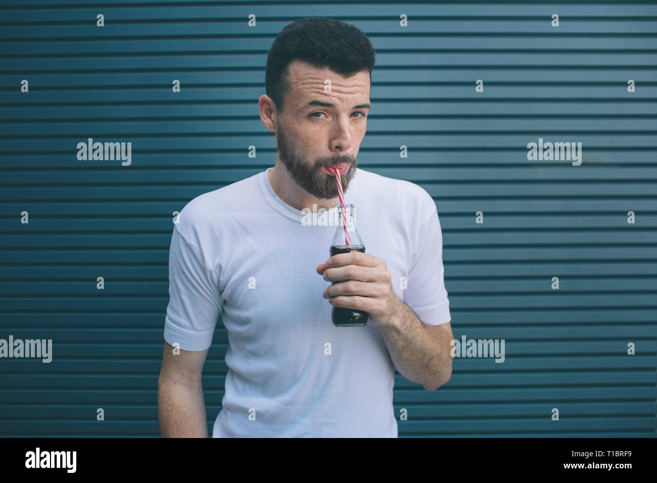 Serious man is drinking cocacola from bottle through straw. He is
