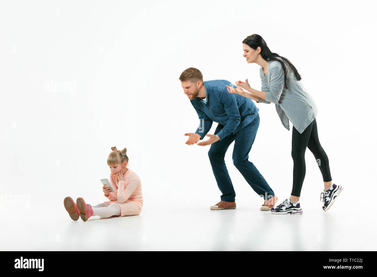 Angry parents scolding their daughter at home. Studio shot of emotional family. Human emotions, childhood, problems, conflict, domestic life, relationship concept Stock Photo