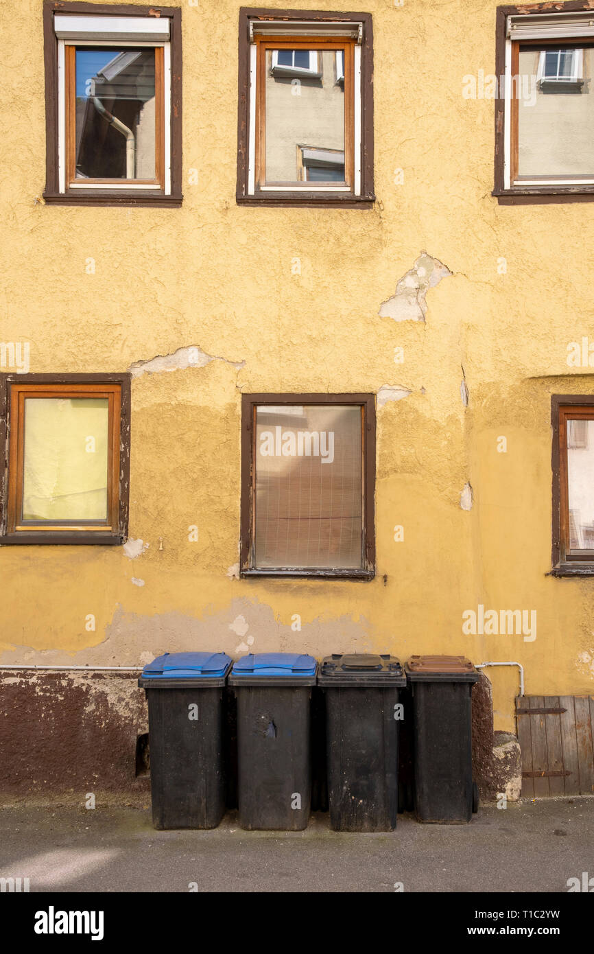different garbage cans in front of an old house whose plaster crumbles