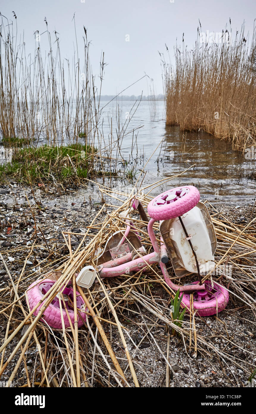 Old pink kids tricycle discarded at a river bank, environment pollution or a crime concept picture. Stock Photo