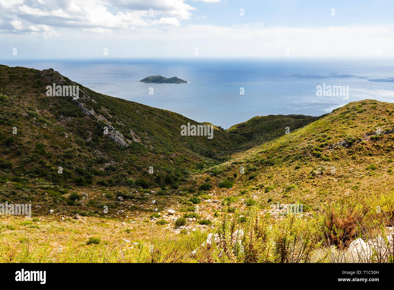 Beautiful view from above on greek bay, blue sky, green hills and small island at blue sea. Colorful summer landscape during sunny day on vacation. Stock Photo