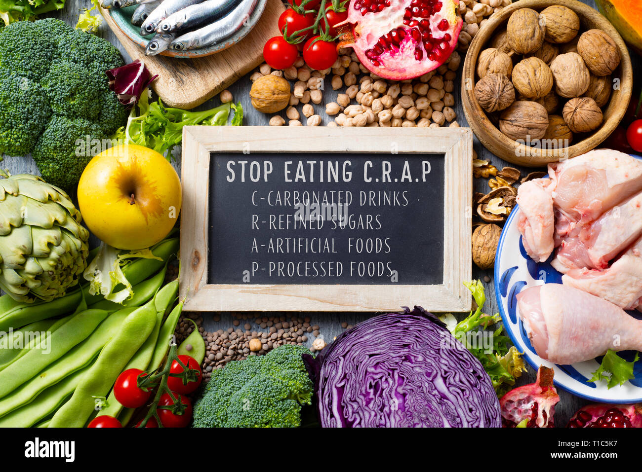 chalkboard with the text stop eating CRAP, for carbonated drinks, refined sugars, artificial foods and processed foods, on a pile of some different ra Stock Photo