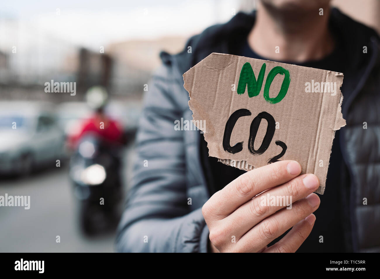 closeup of a young caucasian man, on the street, showing a brown cardboard signboard with the text no CO2 handwritten in it Stock Photo