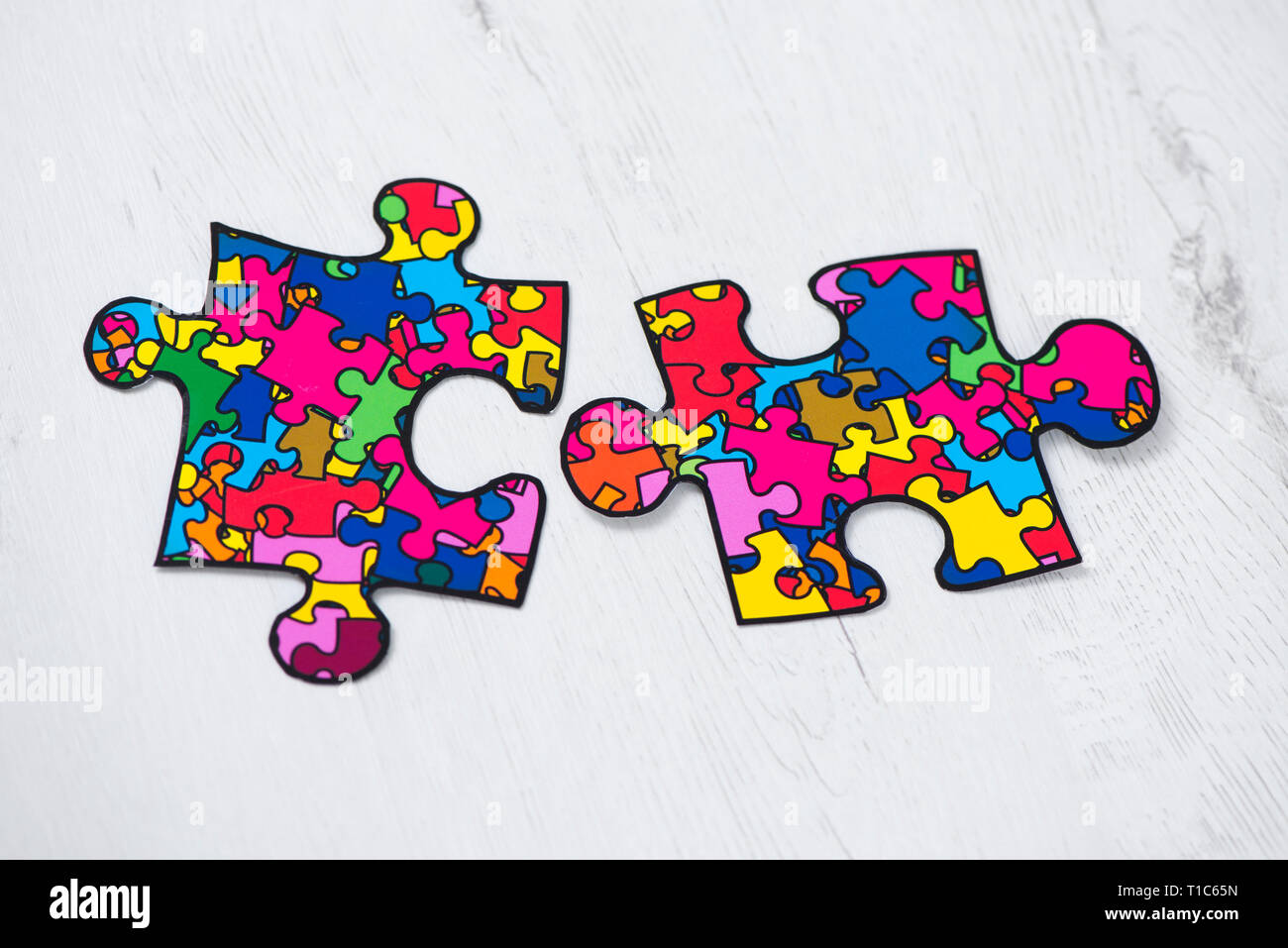two puzzle pieces patterned with many puzzle pieces of different colors, symbol of the autism awareness, on a white rusitc wooden background Stock Photo