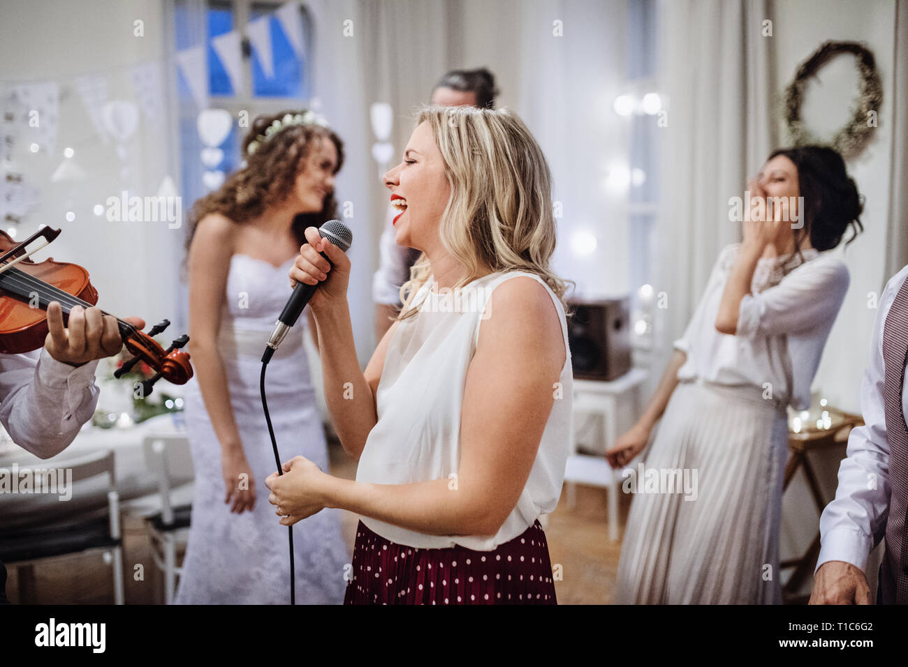 A young woman singing on a wedding reception, bride and guests dancing. Stock Photo