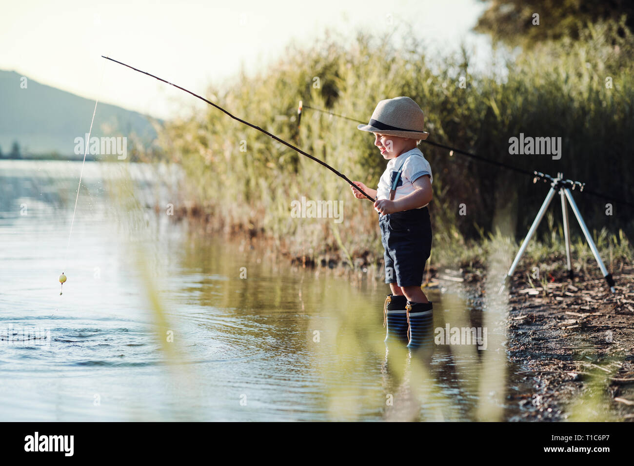 A small toddler boy standing by a lake at sunset, fishing. Copy