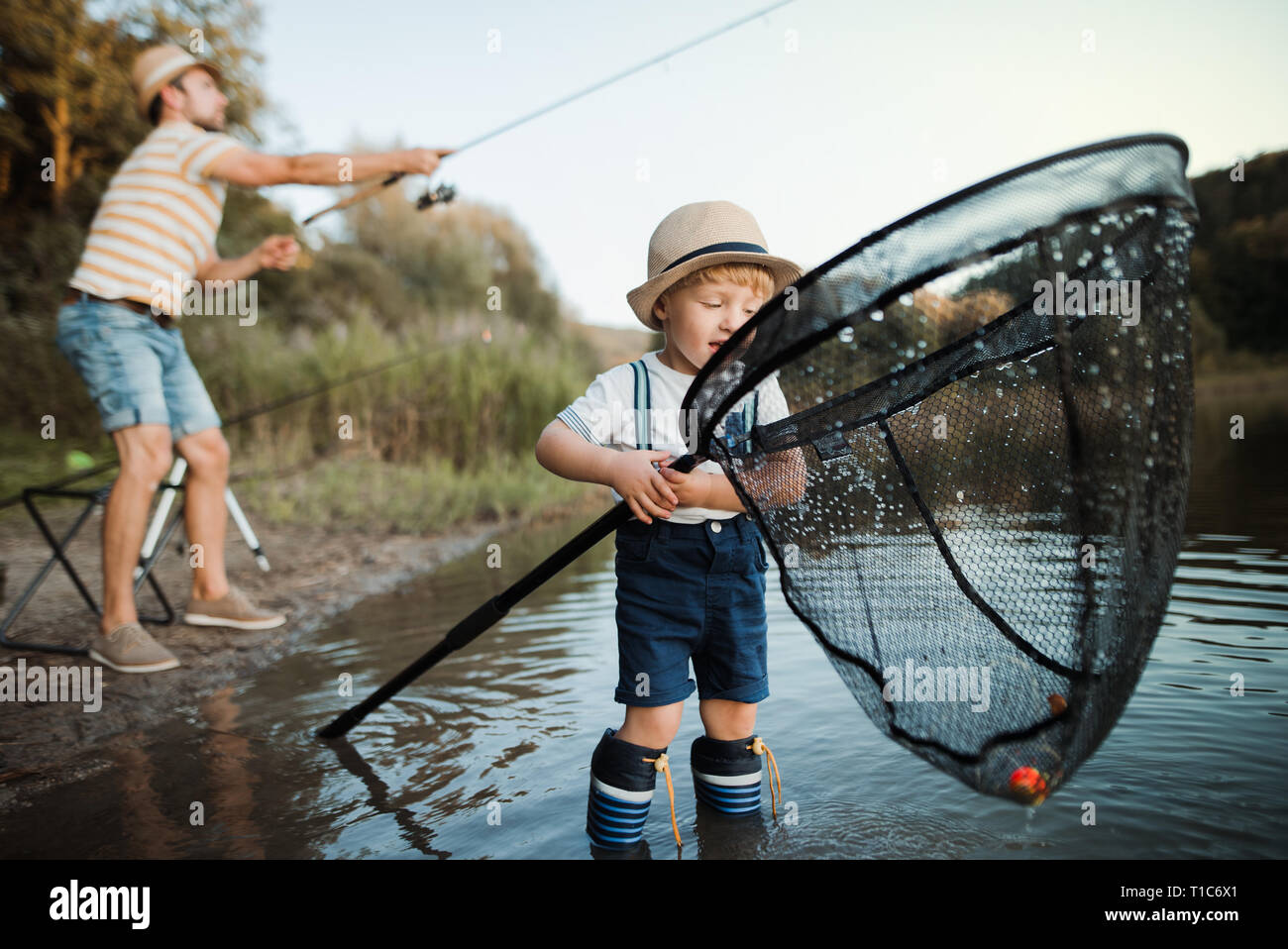 A mature father with a small toddler son outdoors fishing by a lake. Stock Photo