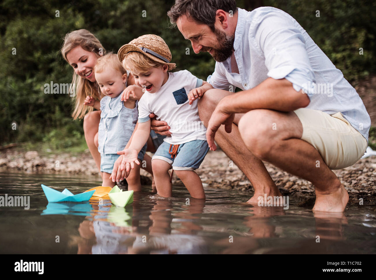 Young family with two toddler children outdoors by the river in summer, playing. Stock Photo