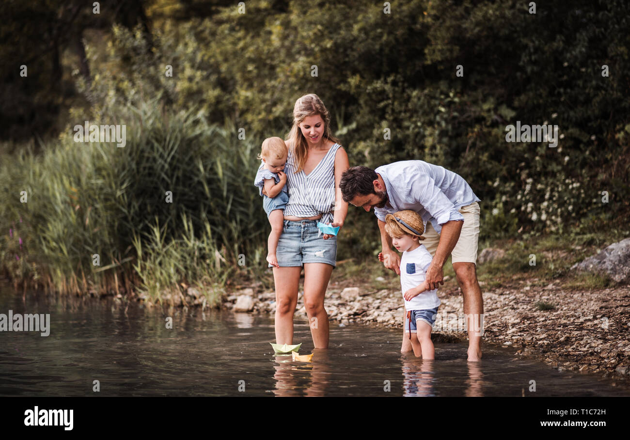 Young family with two toddler children outdoors by the river in summer, playing. Stock Photo