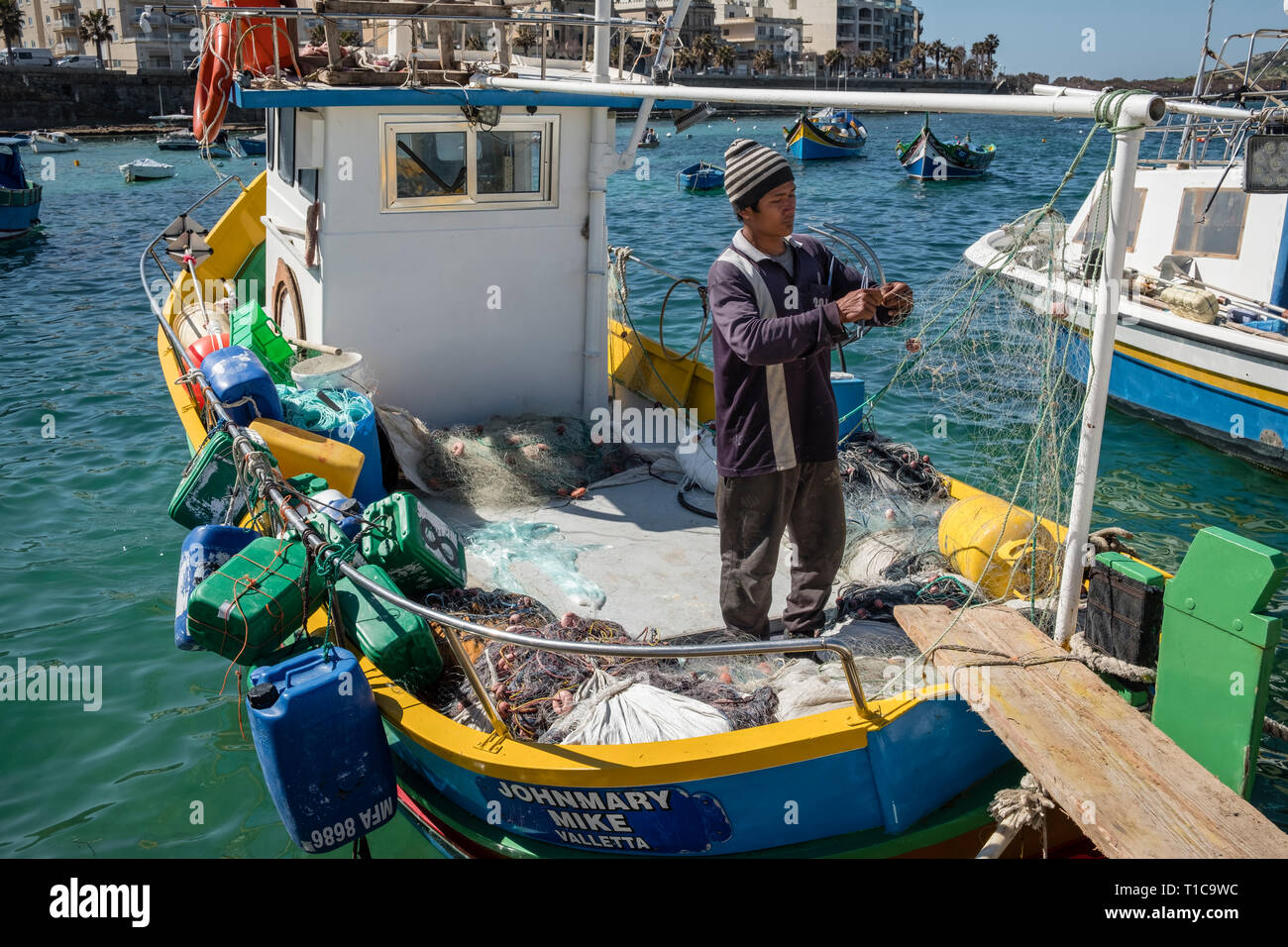 A Fisherman Sorts His Nets On A Traditional Fishing Boat Known As A Luzzu St Paul S Bay Malta Stock Photo Alamy