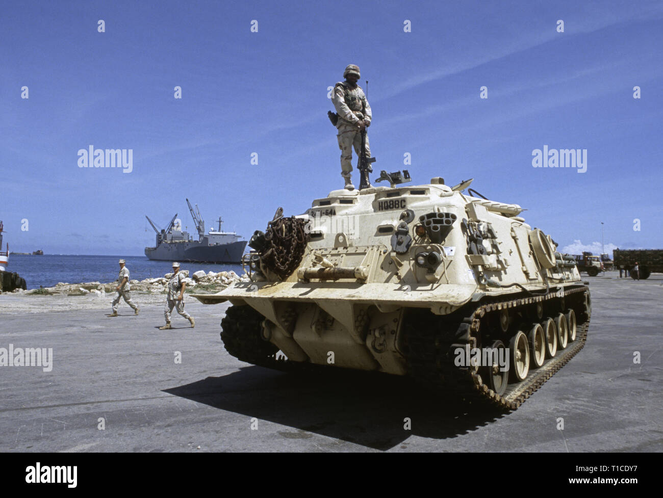 29th October 1993 A U.S. Army soldier of the 24th Infantry Division, 1st Battalion of the 64th Armored Regiment, stands on top of his M88 recovery vehicle, in the port in Mogadishu, Somalia. It has just arrived by sea on board the SS Denebola, which can be seen docked in the background. Stock Photo