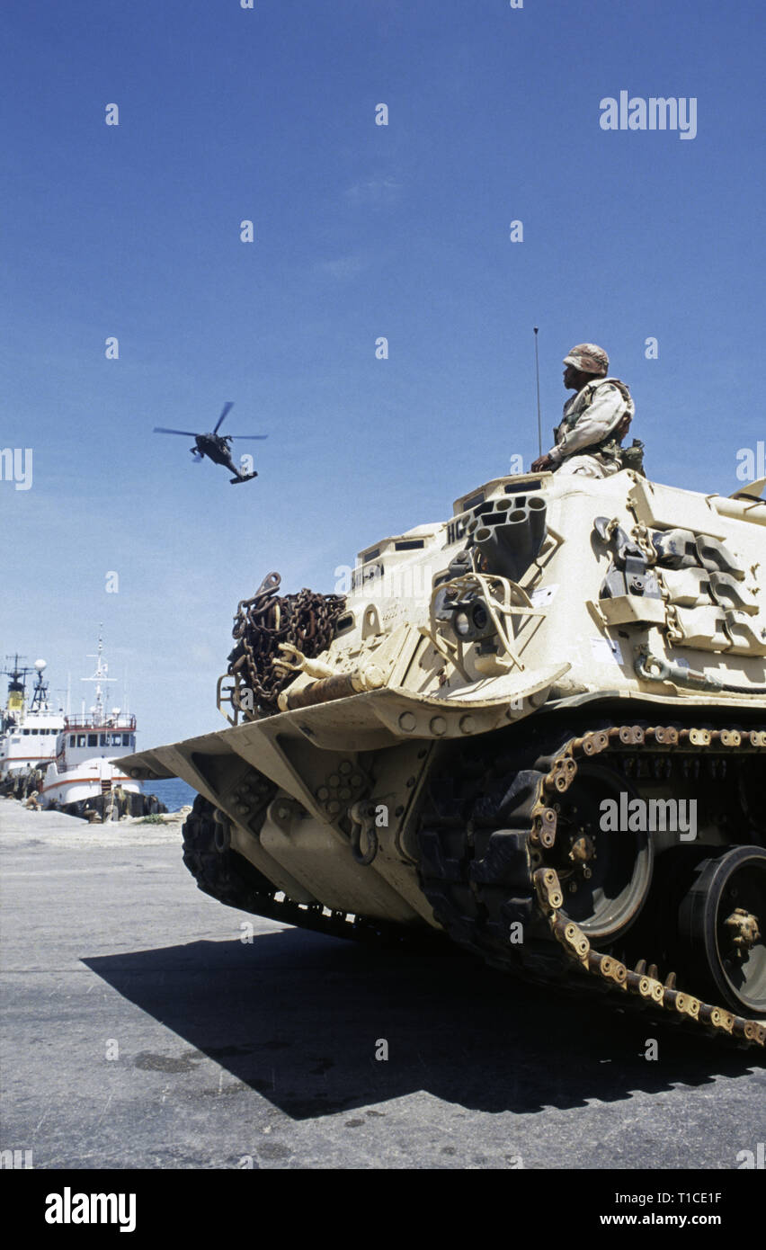 29th October 1993 A U.S. Army soldier of the 24th Infantry Division, 1st Battalion of the 64th Armored Regiment, watches a UH-60 Black Hawk helicopter as he sits on top of his M88 recovery vehicle in the port in Mogadishu, Somalia where it has just arrived by sea. Stock Photo