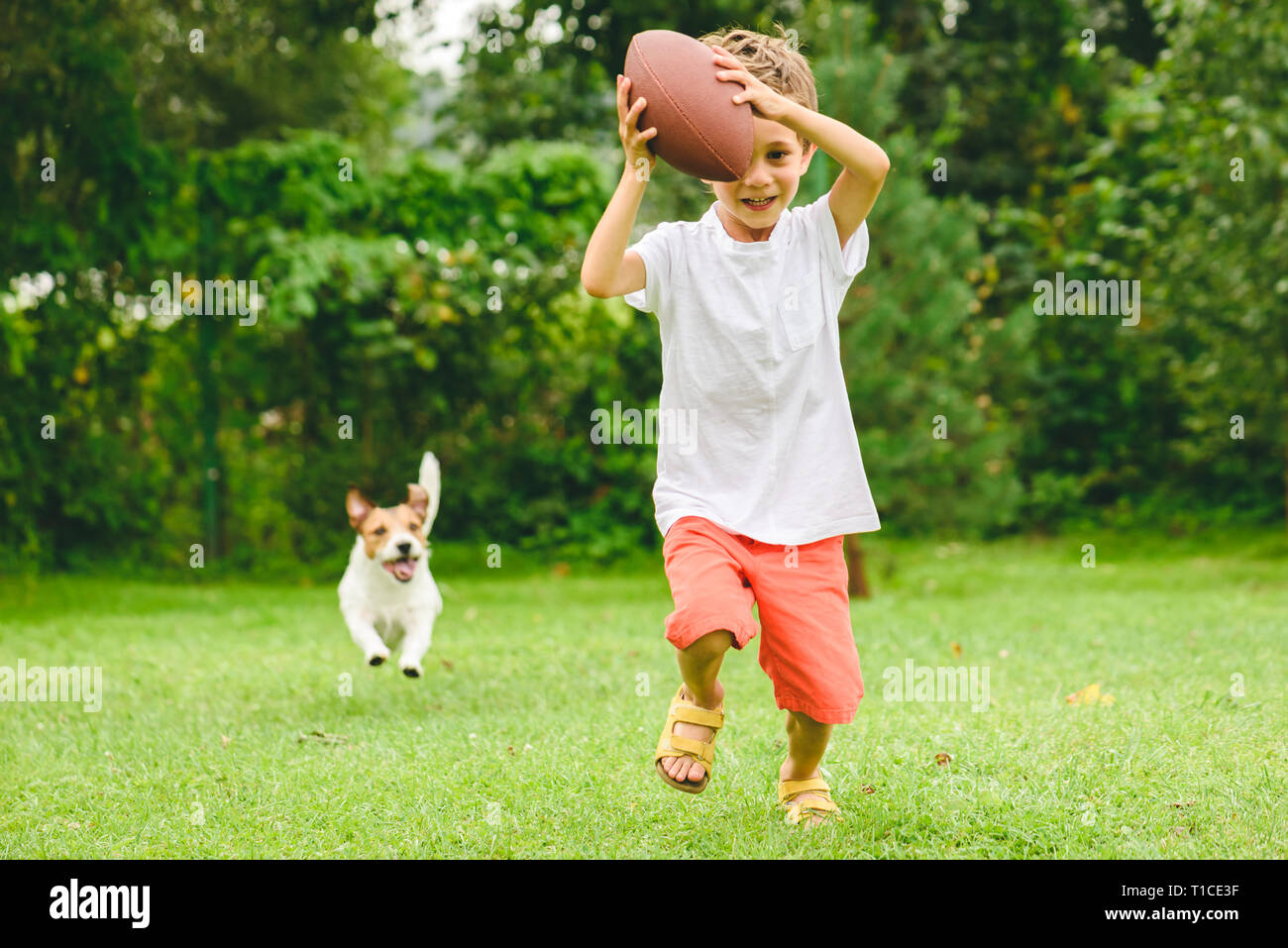 Kid playing american football ready to make touchdown and dog chasing him Stock Photo