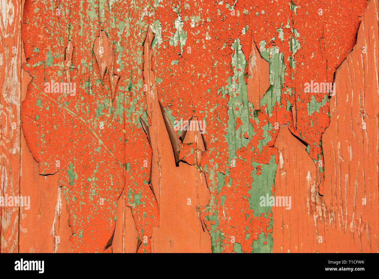 Old orange and green paint flaking off a wooden surface Stock Photo