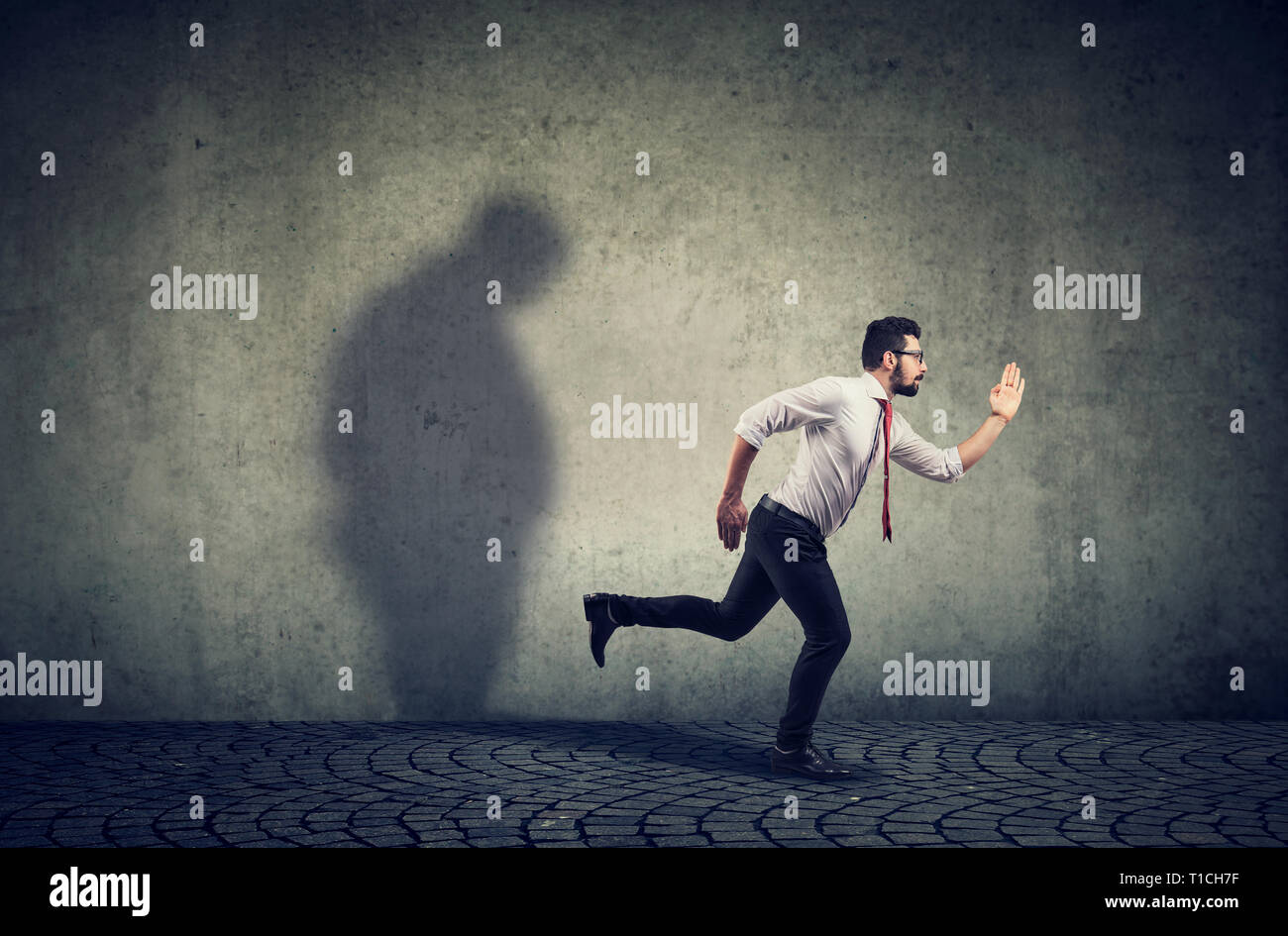 Man running away from his sad gloomy fat shadow on the wall. Mental health and body weight control concept Stock Photo