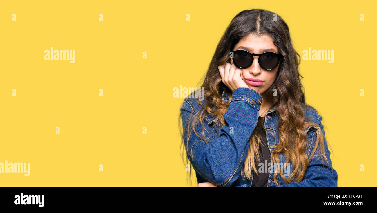 Young beautiful woman wearing sunglasses with hand on chin thinking about question, pensive expression. Smiling with thoughtful face. Doubt concept. Stock Photo