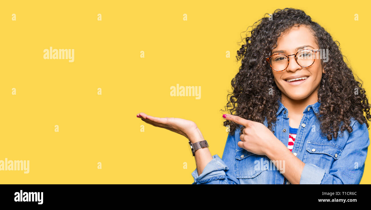 Young beautiful woman with curly hair wearing glasses amazed and ...