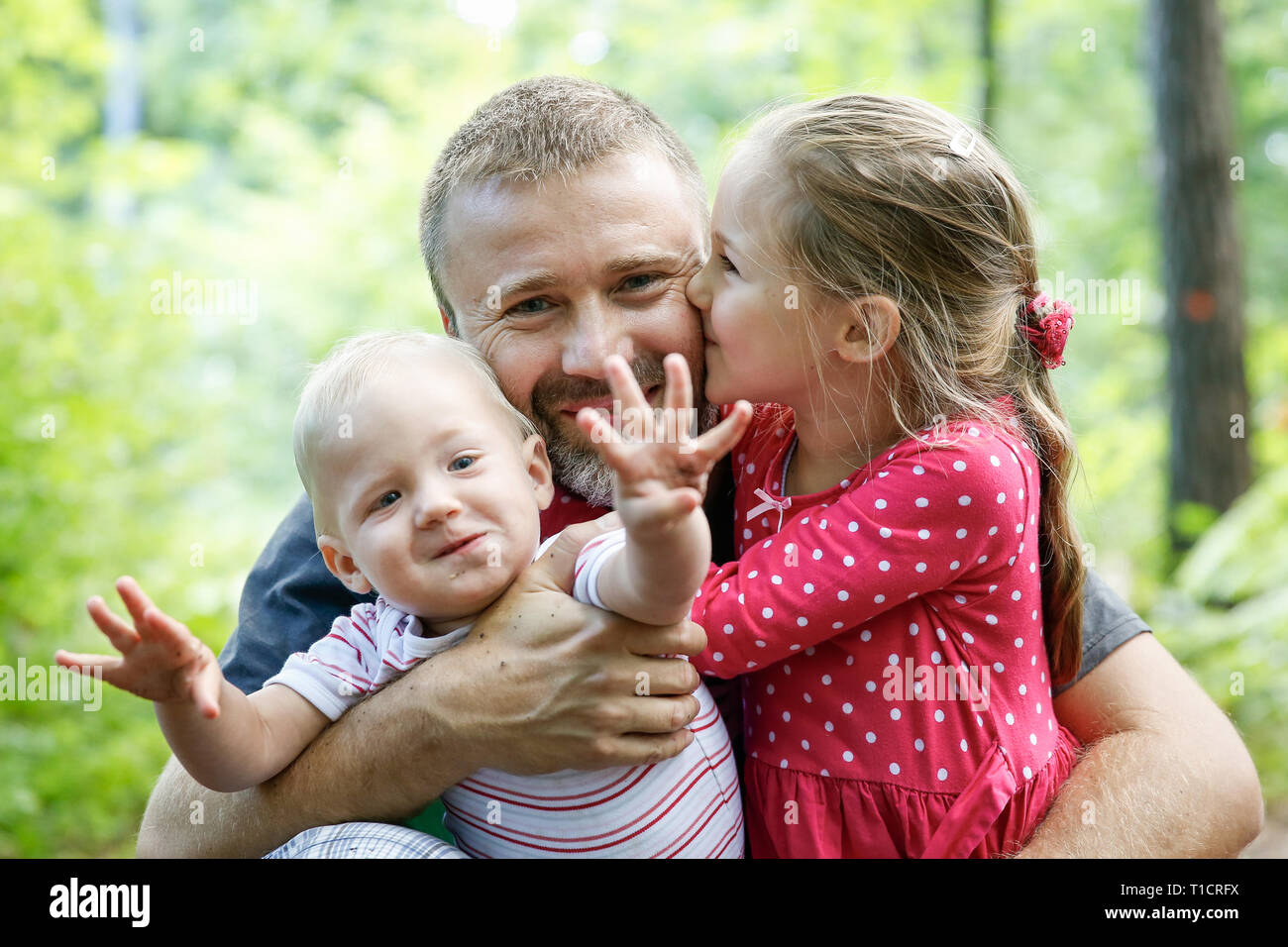 Devoted father hugging his son and daughter, enjoying the outdoor. Family love and bonding, active lifestyle, fathers day concept. Stock Photo